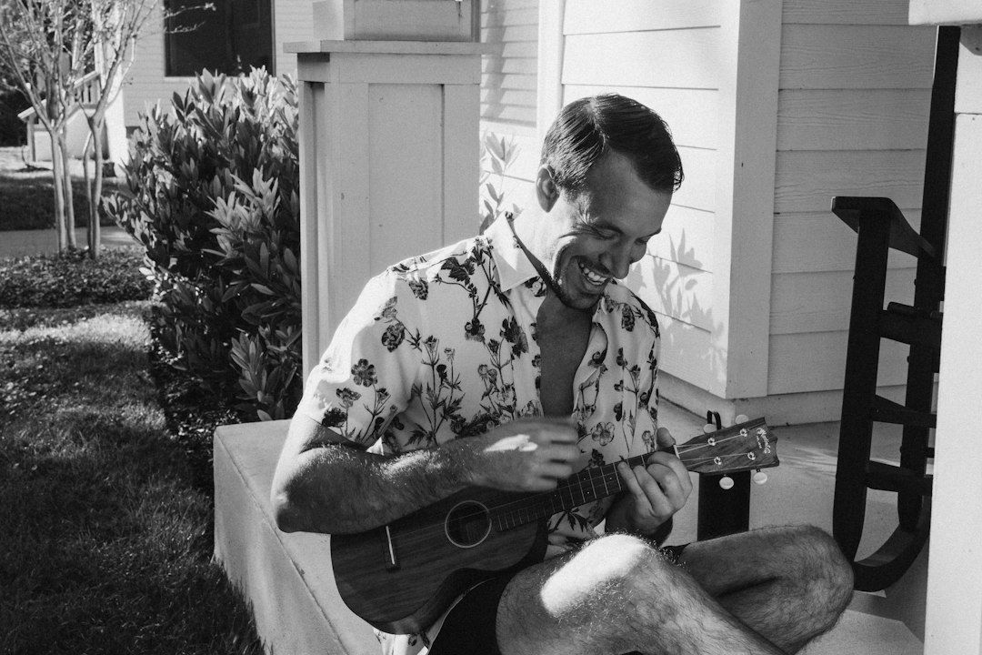 Man playing a small acoustic guitar on a sunny front porch
